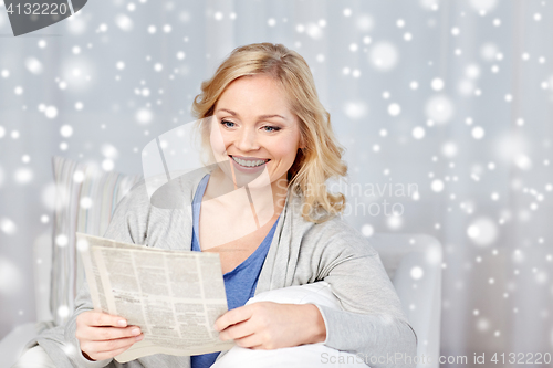 Image of smiling woman reading newspaper at home