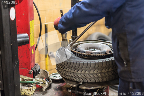 Image of Professional auto mechanic replacing tire on wheel in car repair service.