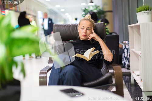 Image of Charming girl sitting by wooden table and reading book