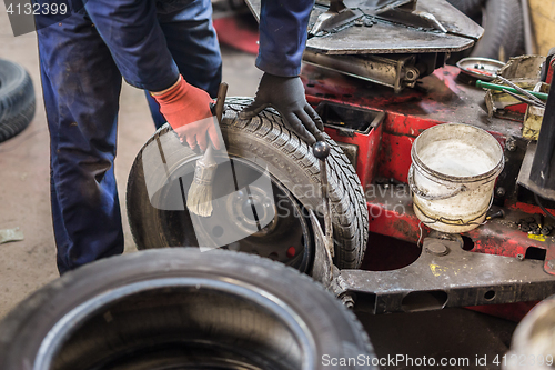 Image of Professional auto mechanic replacing tire on wheel in car repair service.