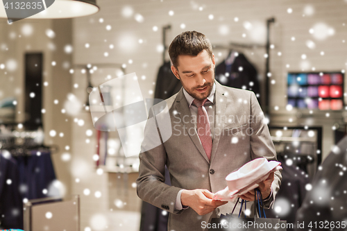 Image of happy young man choosing shirt in clothing store