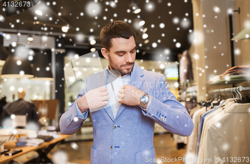 Image of happy young man trying jacket on in clothing store