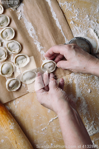 Image of woman folds the raw dumplings on a sheet of parchment