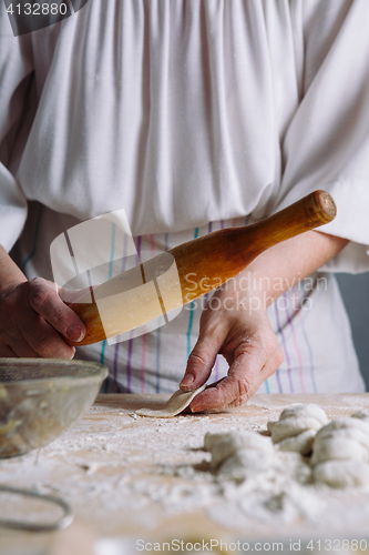 Image of Making meat dumpling with wooden rolling pin.