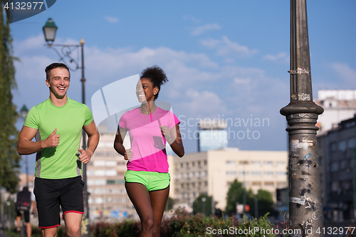 Image of young smiling multiethnic couple jogging in the city