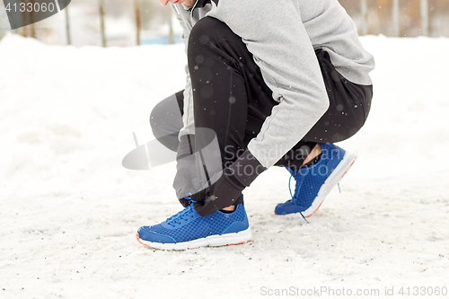 Image of man with earphones tying sports shoes in winter