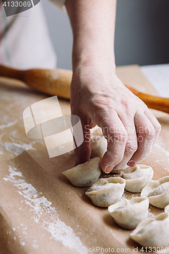 Image of woman folds the raw dumplings on a sheet of parchment