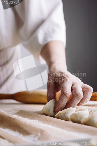 Image of woman folds the raw dumplings on a sheet of parchment