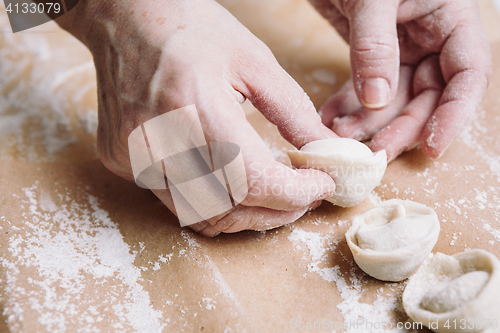 Image of woman folds the raw dumplings on a sheet of parchment