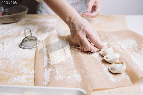 Image of woman folds the raw dumplings on a sheet of parchment