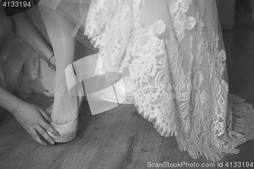 Image of bridesmaid helping bride to put on elegant shoes. Black and white shot