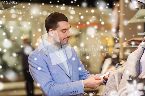 Image of happy young man choosing clothes in clothing store