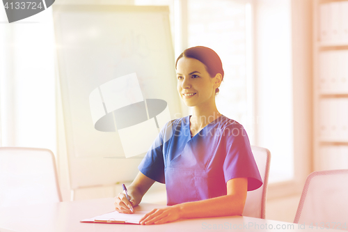 Image of happy female doctor or nurse writing to clipboard