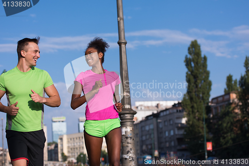 Image of young smiling multiethnic couple jogging in the city