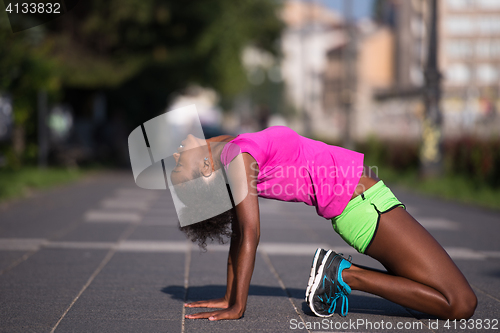 Image of sporty young african american woman stretching outdoors