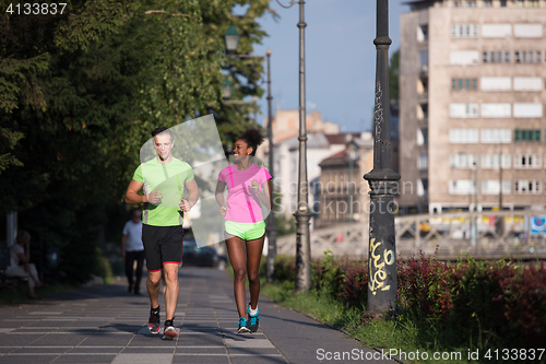 Image of young smiling multiethnic couple jogging in the city