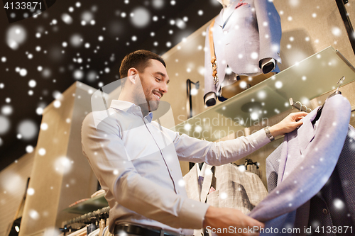 Image of happy young man choosing clothes in clothing store