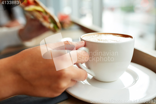 Image of woman drinking coffee and eating sandwich at cafe