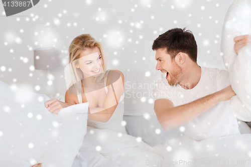 Image of happy couple having pillow fight in bed at home