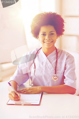 Image of happy female doctor or nurse writing to clipboard