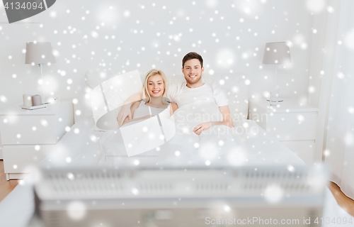 Image of happy couple lying in bed at home and watching tv