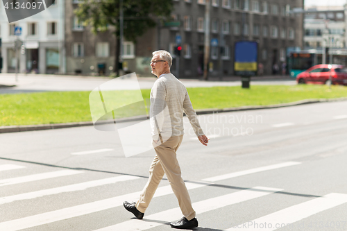 Image of senior man walking along city crosswalk