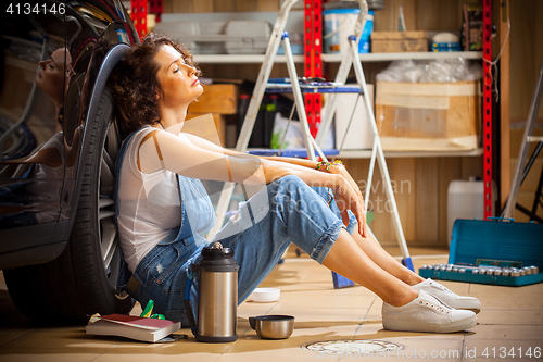 Image of auto mechanic woman in blue overalls resting near the wheel of t