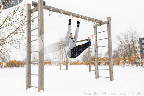 Image of young man exercising on horizontal bar in winter