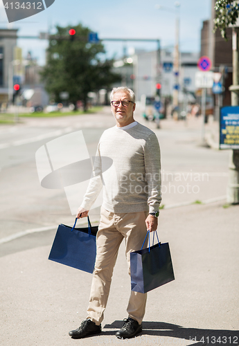 Image of senior man with shopping bags walking in city