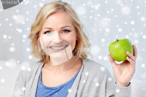 Image of happy middle aged woman with green apple at home