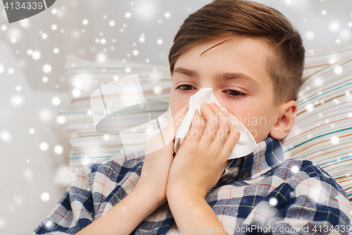 Image of close up of ill boy lying in bed and blowing nose