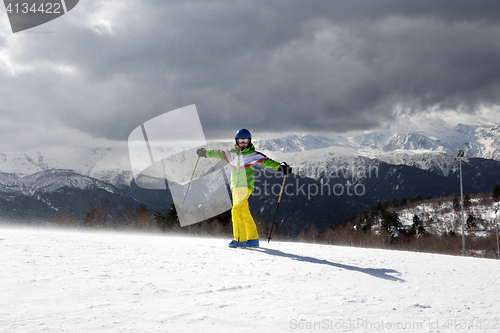 Image of Happy young skier with ski poles in sun mountains and cloudy gra