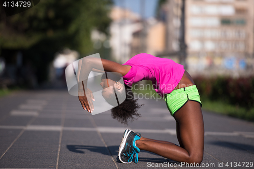 Image of sporty young african american woman stretching outdoors