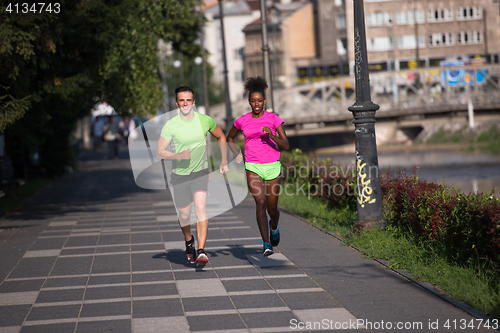 Image of young smiling multiethnic couple jogging in the city