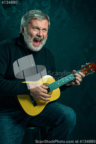 Image of Studio portrait of senior man with guitar.