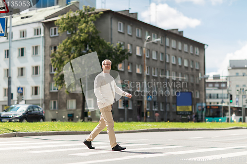 Image of senior man walking along city crosswalk