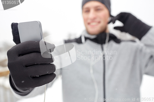 Image of happy man with earphones and smartphone in winter