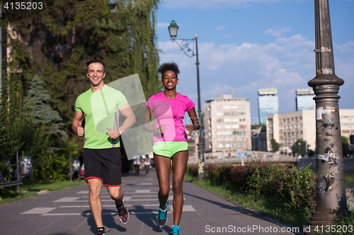 Image of young smiling multiethnic couple jogging in the city