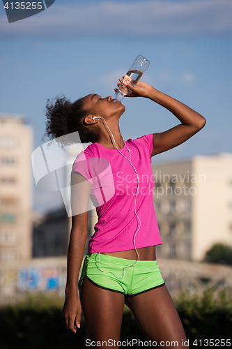 Image of african american woman drinking water after jogging