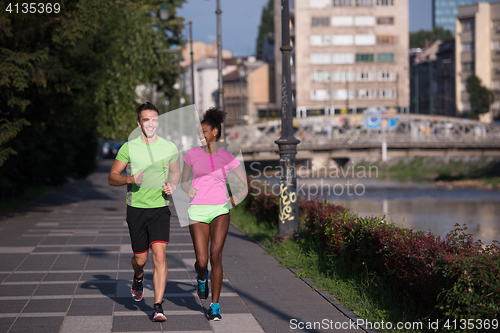 Image of young smiling multiethnic couple jogging in the city