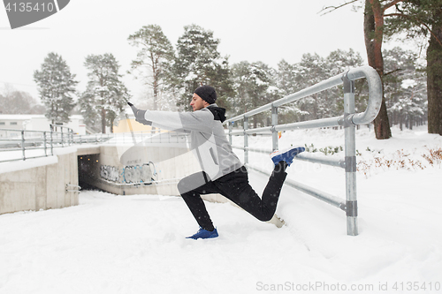 Image of sports man stretching leg at fence in winter