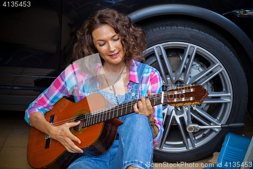 Image of woman car mechanic with guitar in garage