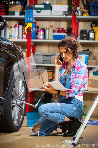 Image of car mechanic woman in blue overalls talking on the phone near a 