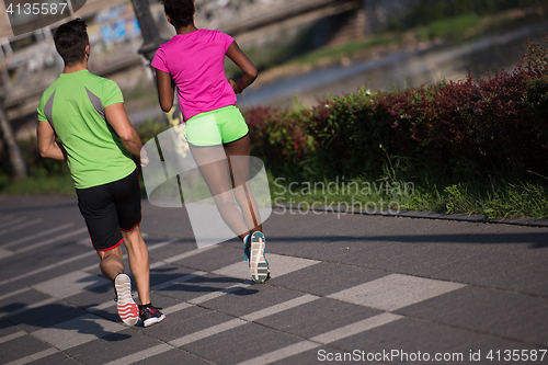 Image of young smiling multiethnic couple jogging in the city