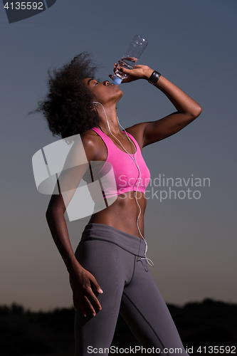 Image of african american woman drinking water after jogging in nature