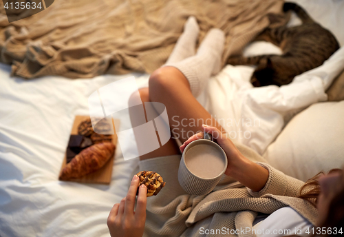 Image of close up of woman with cocoa cup and cookie in bed