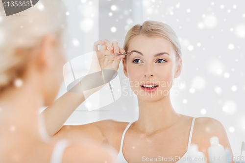 Image of woman with tweezers tweezing eyebrow at bathroom