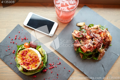 Image of goat cheese and ham salads with smartphone at cafe