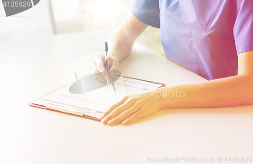 Image of close up of doctor or nurse writing to clipboard