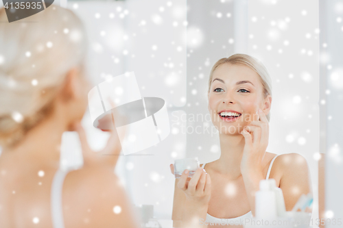Image of happy woman applying cream to face at bathroom